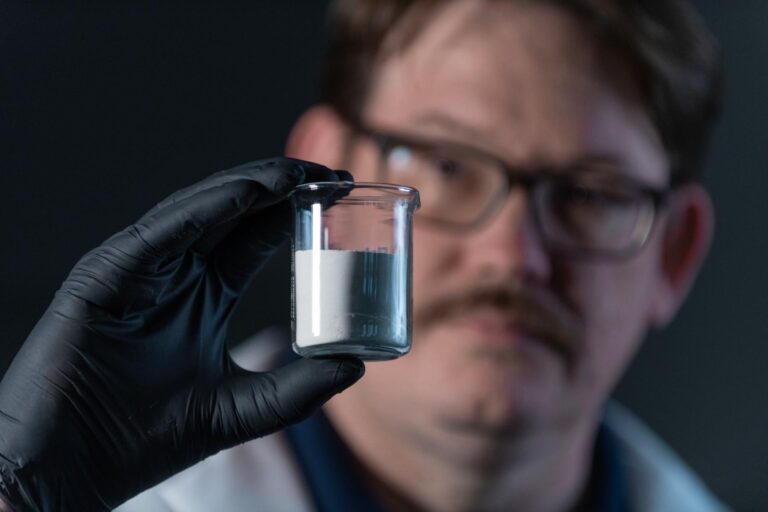 Scientist holding a glass vile of powdered SureCure.