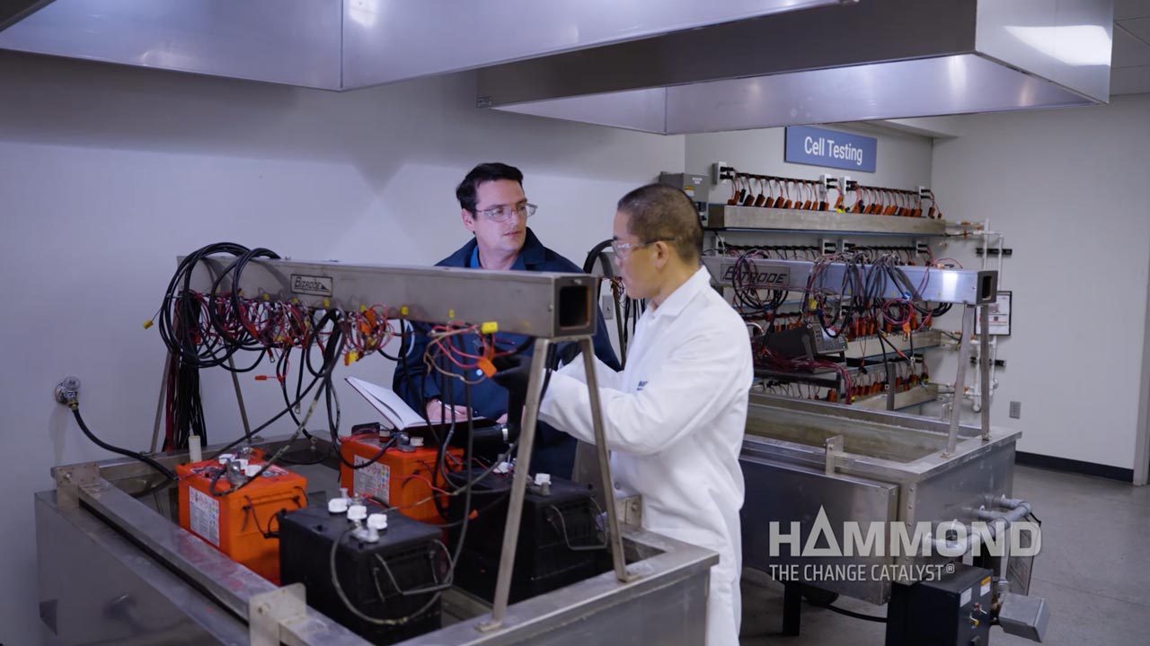 two men in lab coats testing batteries on metal table